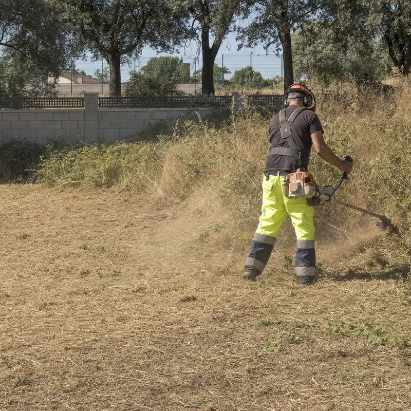 Operario con desbrozadora despejando la hierba seca de una parcela